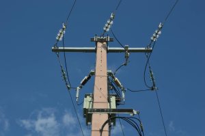Low angle view of a utility pole with power lines against a blue sky.