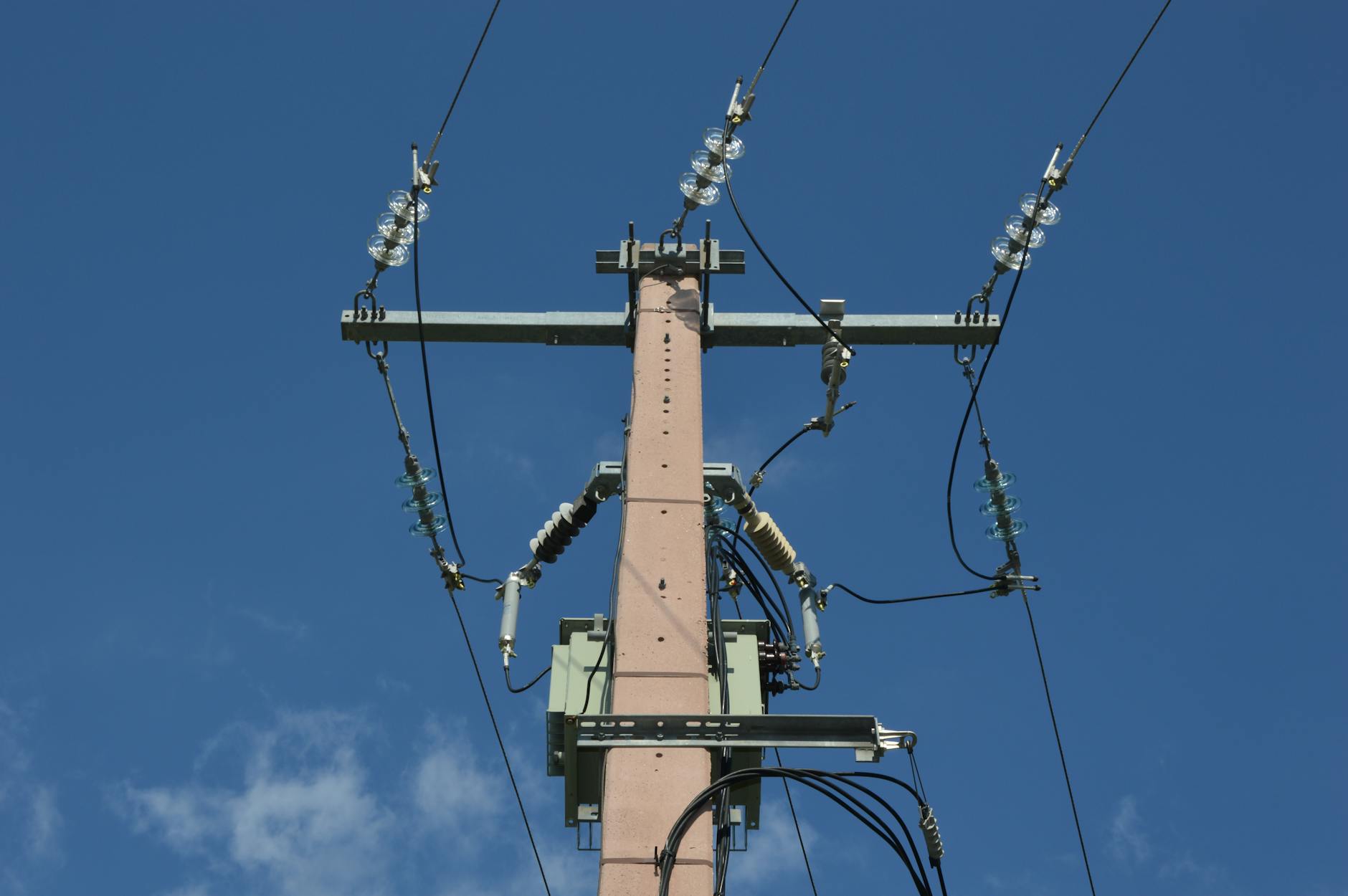 Low angle view of a utility pole with power lines against a blue sky.