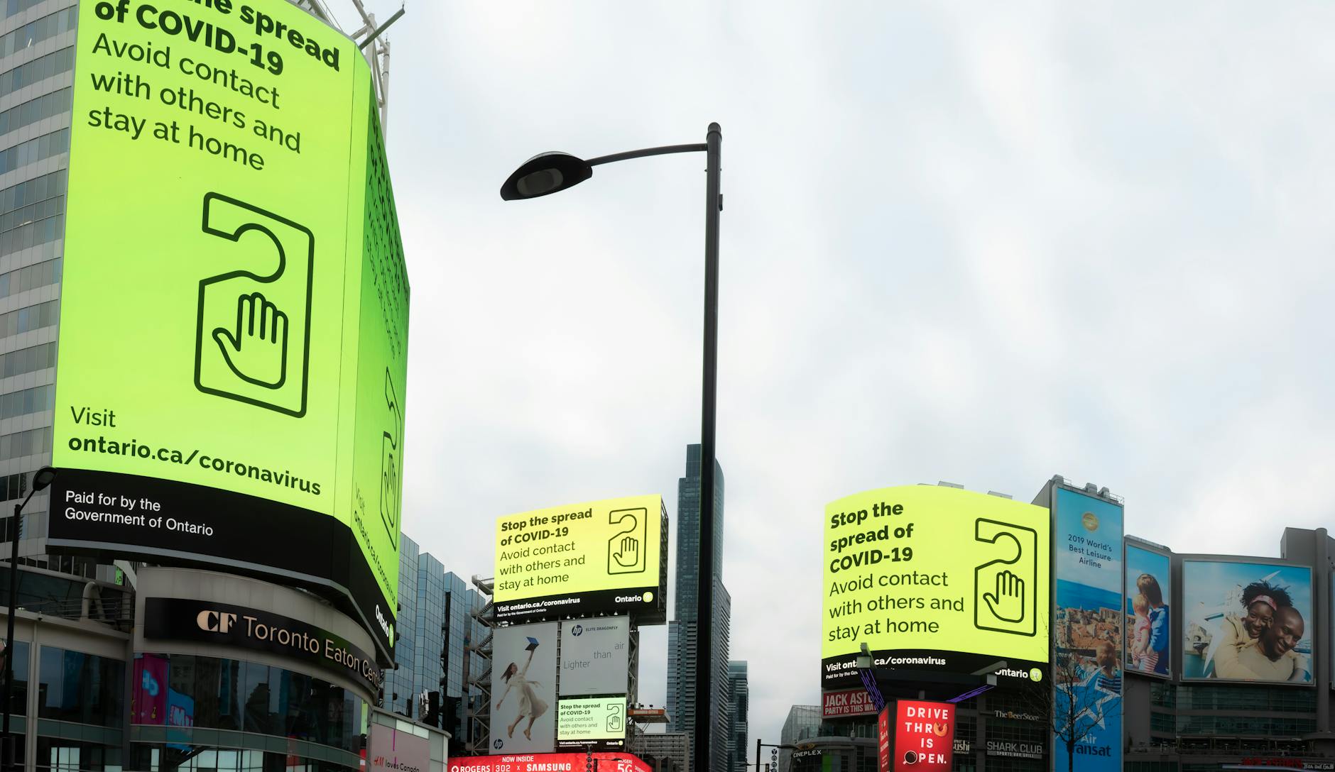 From below of modern buildings with billboards about coronavirus located on on city street under cloudy sky