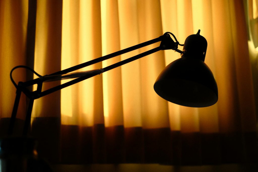 Dramatic silhouette of a desk lamp with warm backlighting from yellow curtains.