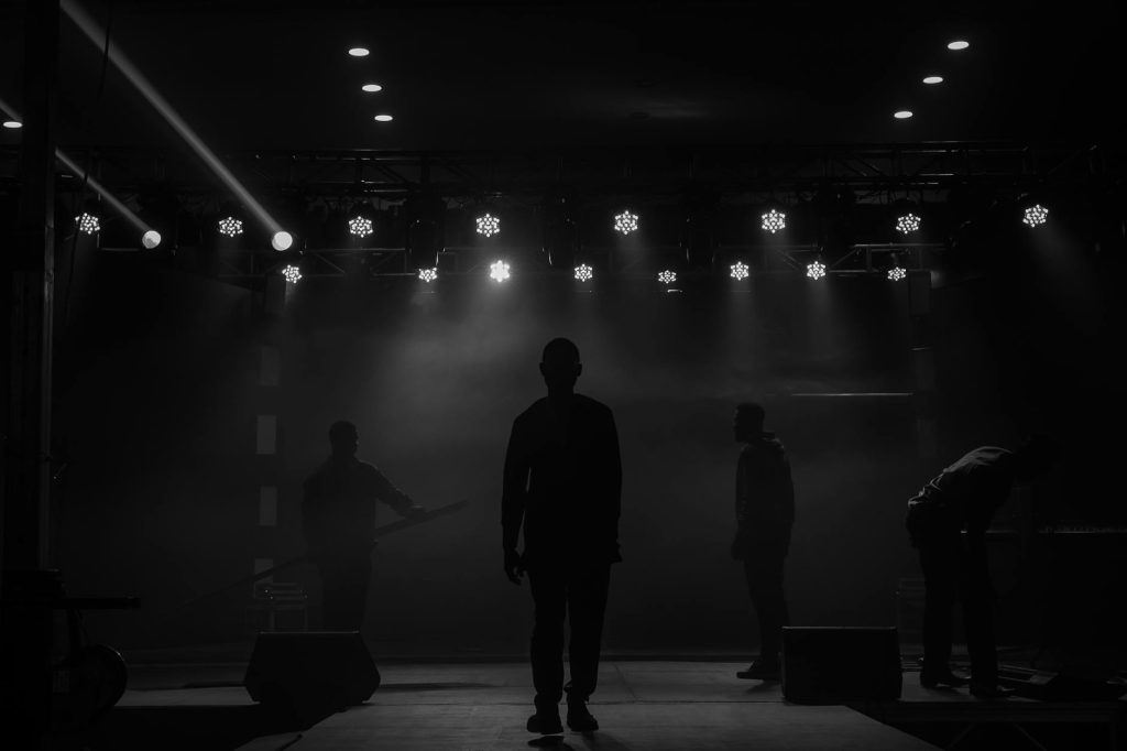 A dramatic stage scene in Ibadan, Nigeria with silhouetted figures under bright lights.