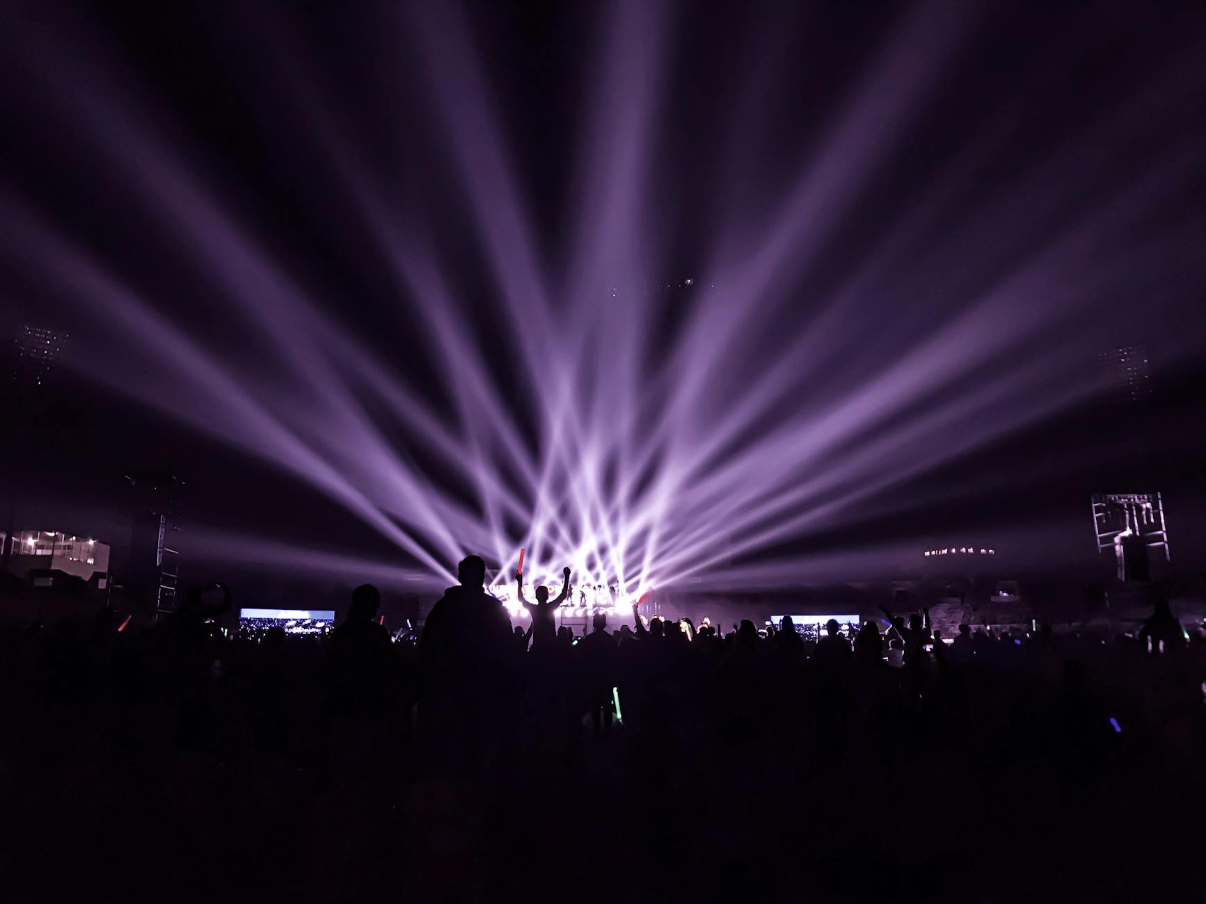 A lively night concert with beams of colorful lights and an energetic crowd.