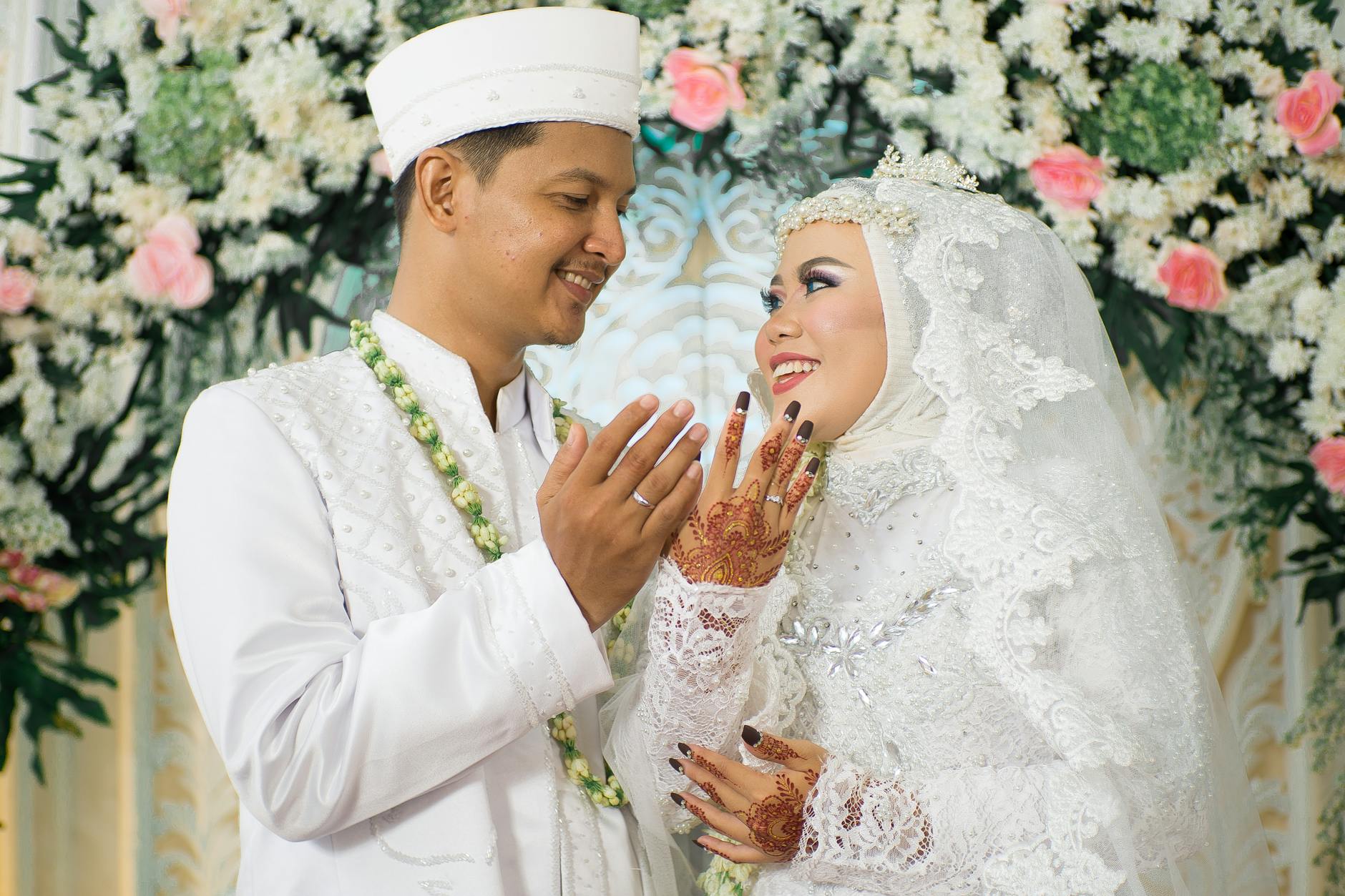Asian bride and groom in traditional attire, with henna, amidst floral decor.