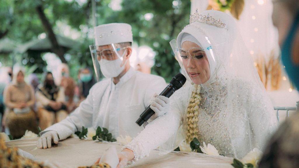 A bride and groom in protective face shields during a traditional wedding ceremony, embracing new norms of safety.