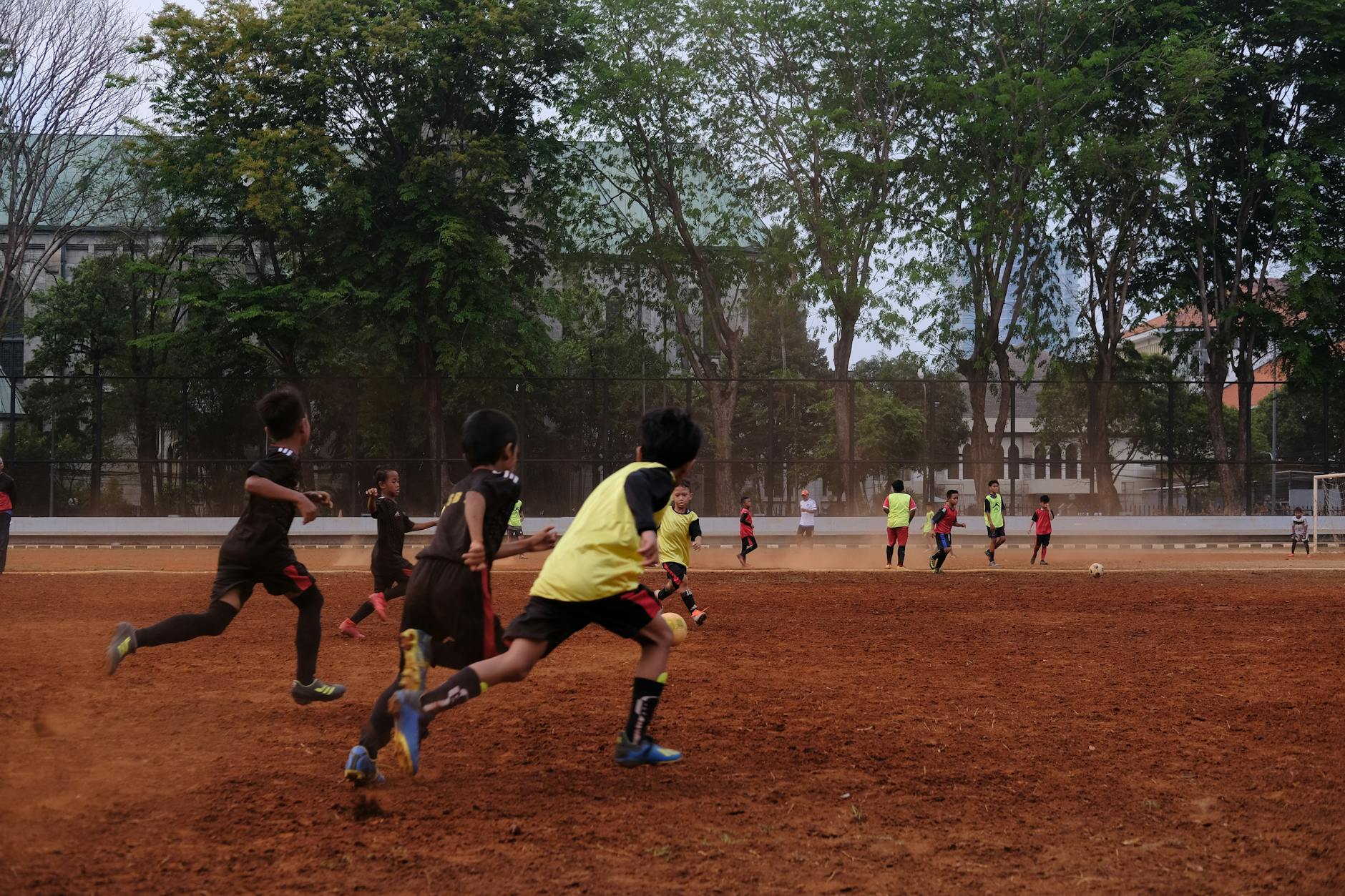 Group of kids playing soccer on a dirt field with trees in background, showcasing teamwork and sportsmanship.