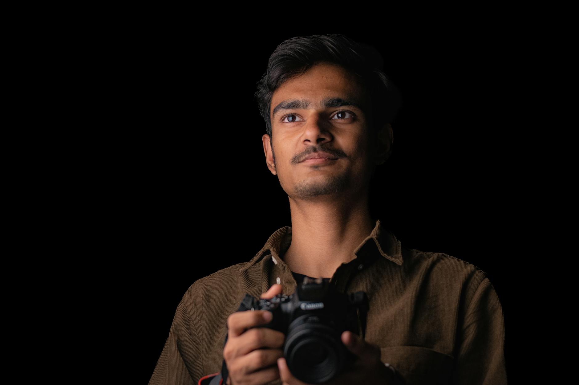 Portrait of a young man holding a DSLR camera in a dark studio setting.