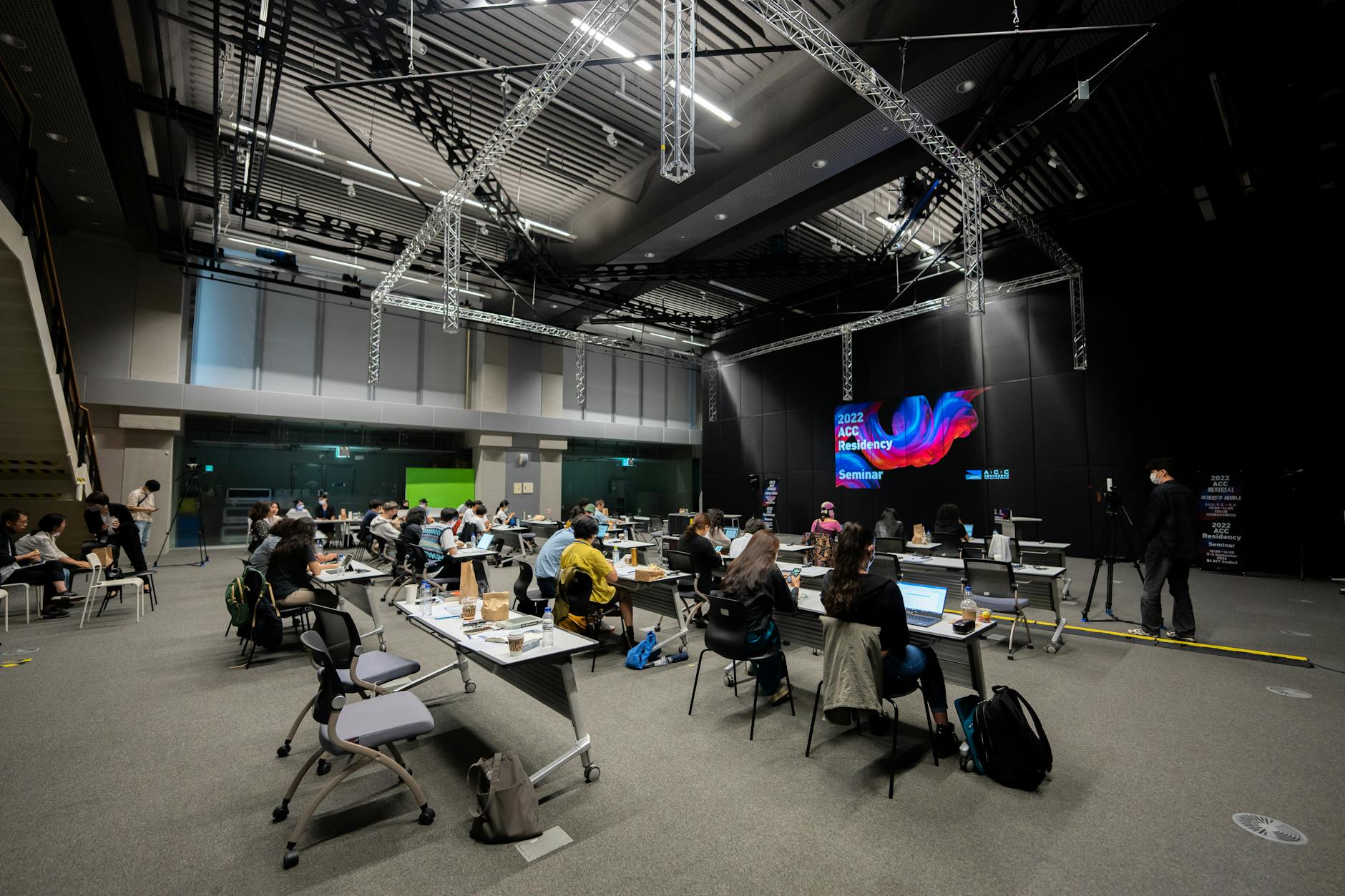 A diverse group attending an educational seminar with screens and seating indoors, highlighting collaboration.