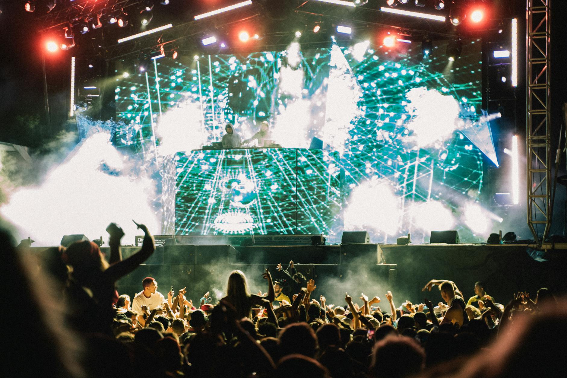 Vibrant music concert with DJ and crowd at night, showcasing lively atmosphere and dazzling lights.
