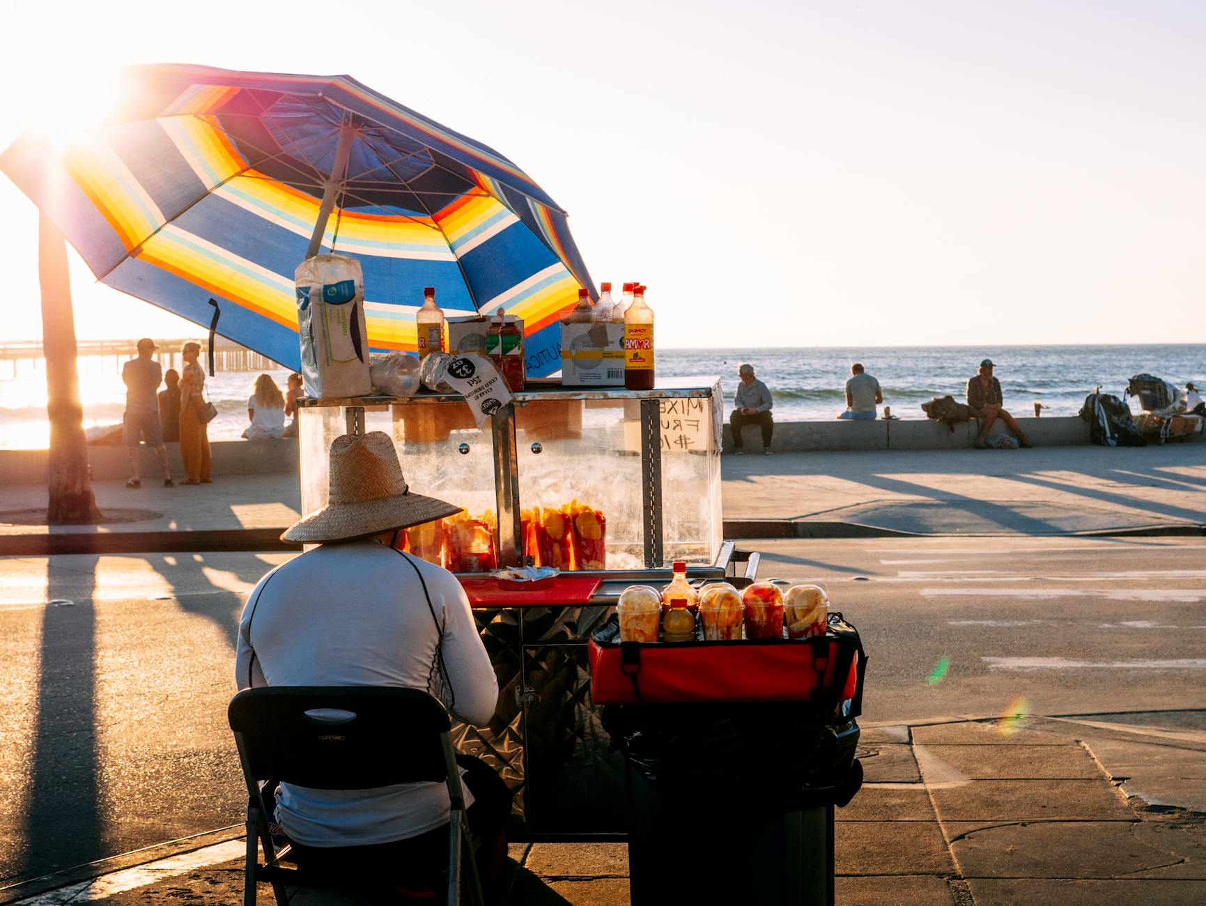 Vibrant fruit vendor with umbrella, near the San Diego beach, bathed in sunset light.