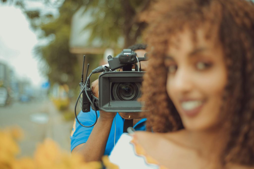 Woman smiling near videographer with camera, outdoors during the day capturing vibrant, natural moments.