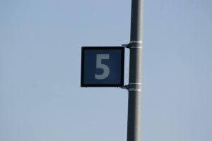 Close-up of metal pole with number 5 sign against a clear blue sky.