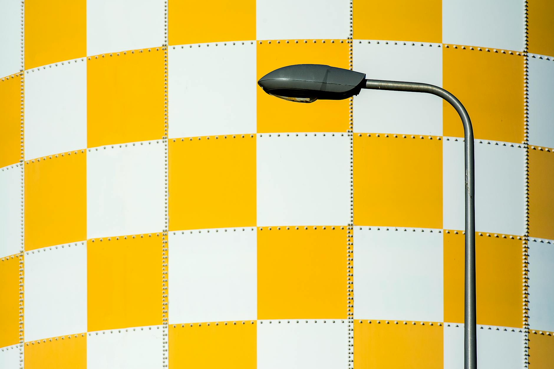 Street lamp in front of a yellow and white checkered wall with ample copyspace.