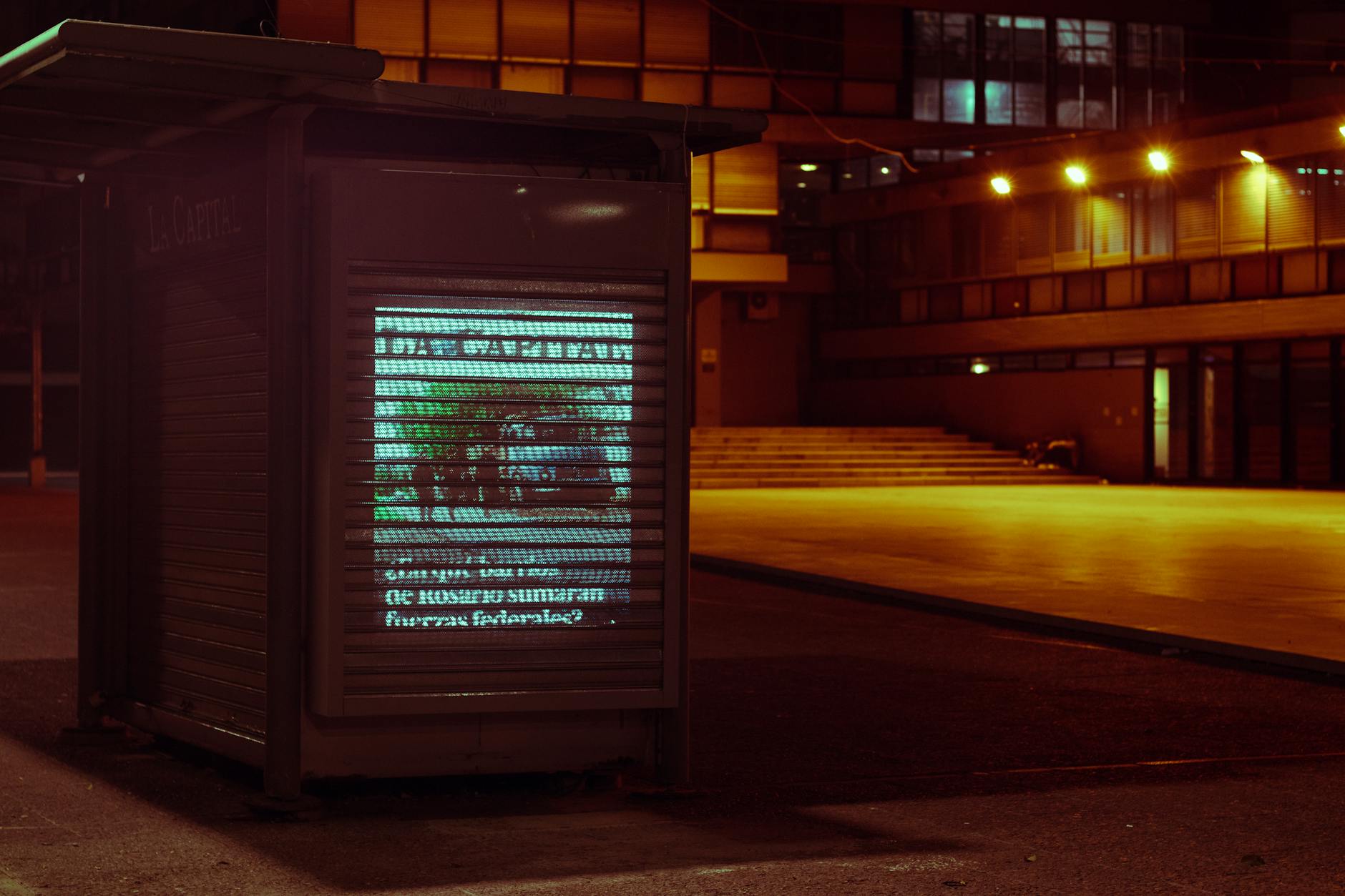 Dimly lit urban scene at night with a lighted display on the street in Rosario, Argentina.