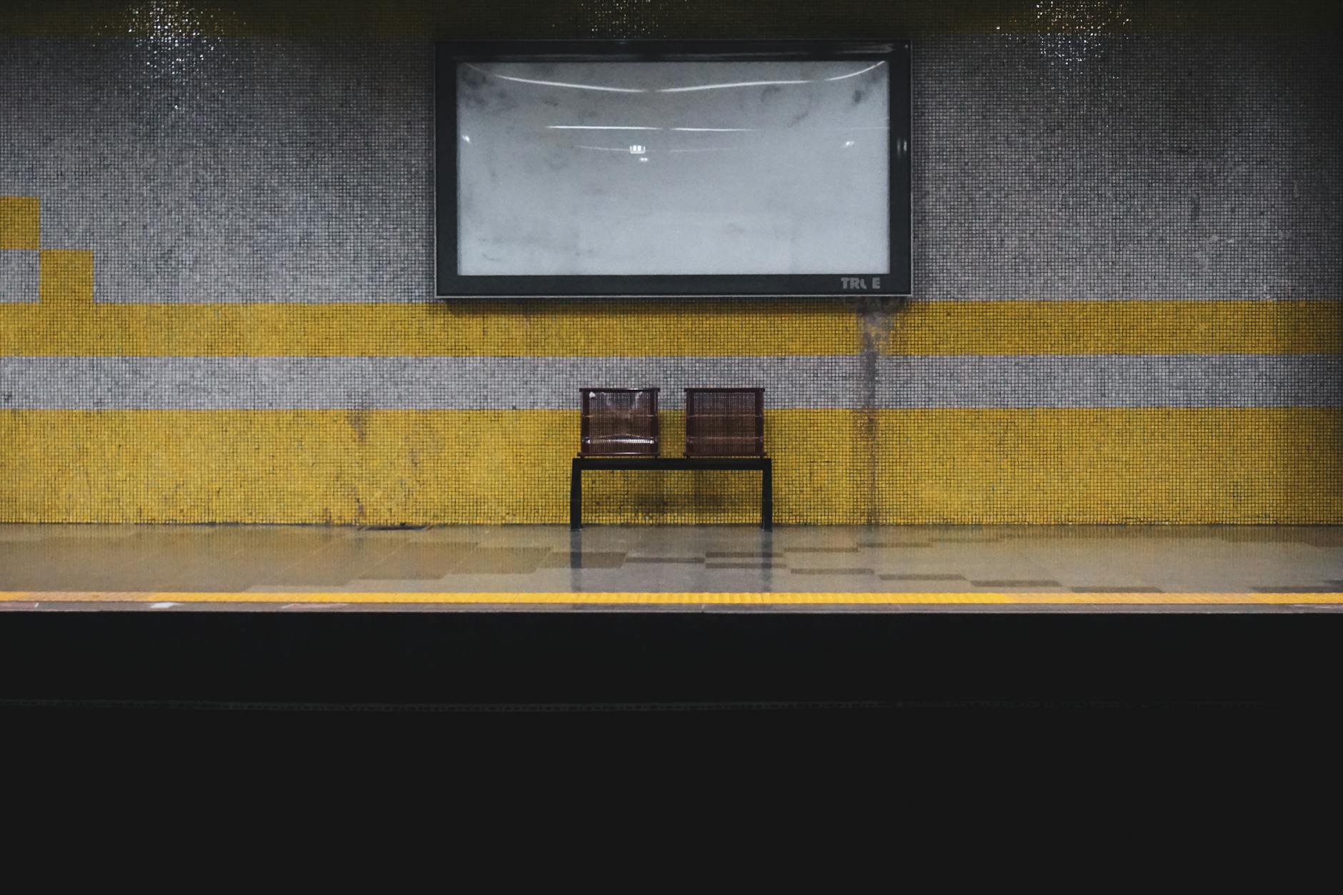 A deserted subway platform featuring a modern bench against a tiled background.