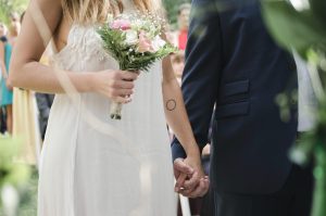 Beautiful outdoor wedding ceremony showcasing a bride and groom holding hands with a bouquet of flowers.