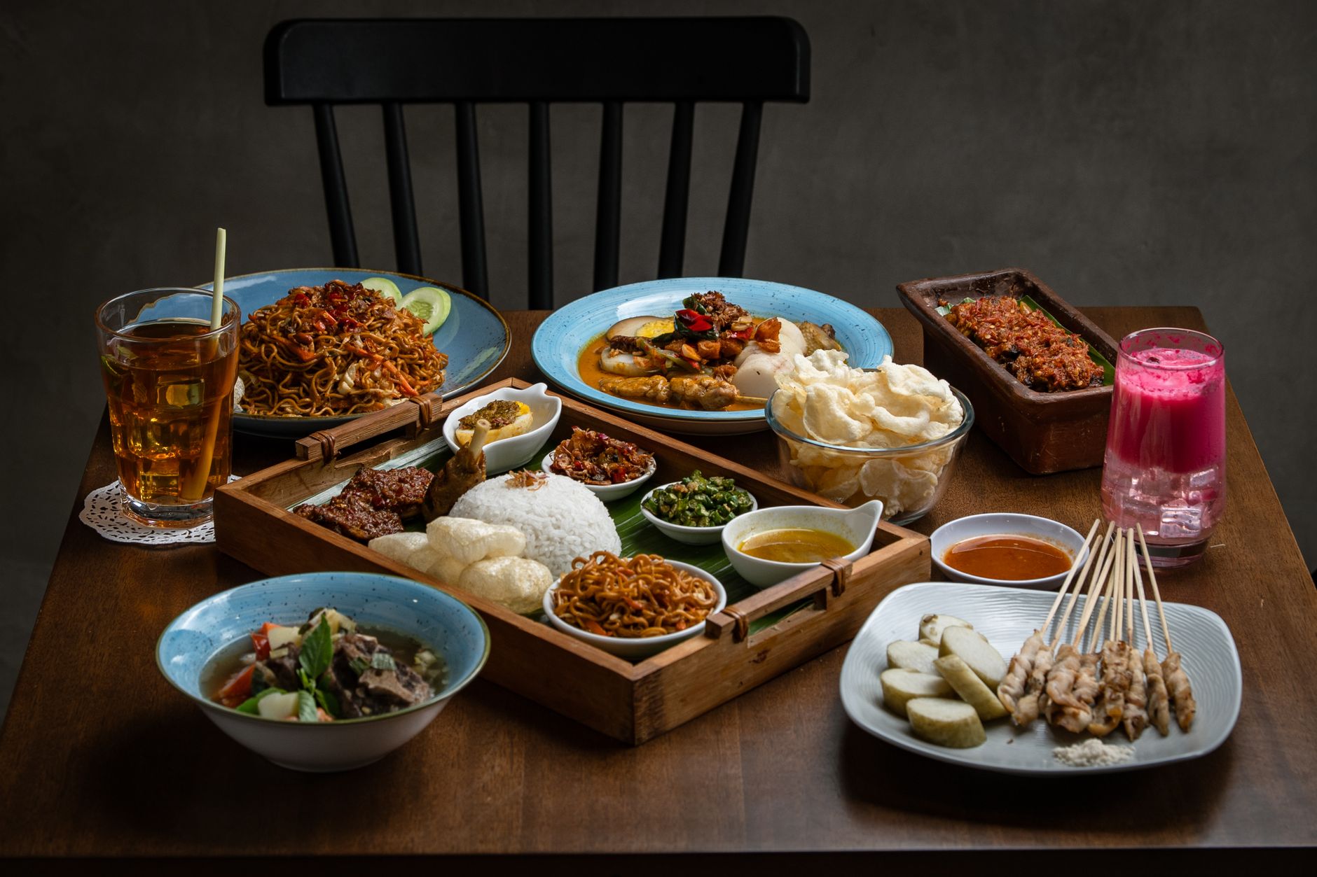 A variety of Indonesian dishes including satay, noodles, and rice served indoors.