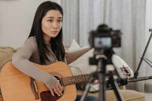 Asian woman playing acoustic guitar during an online music lesson at home.
