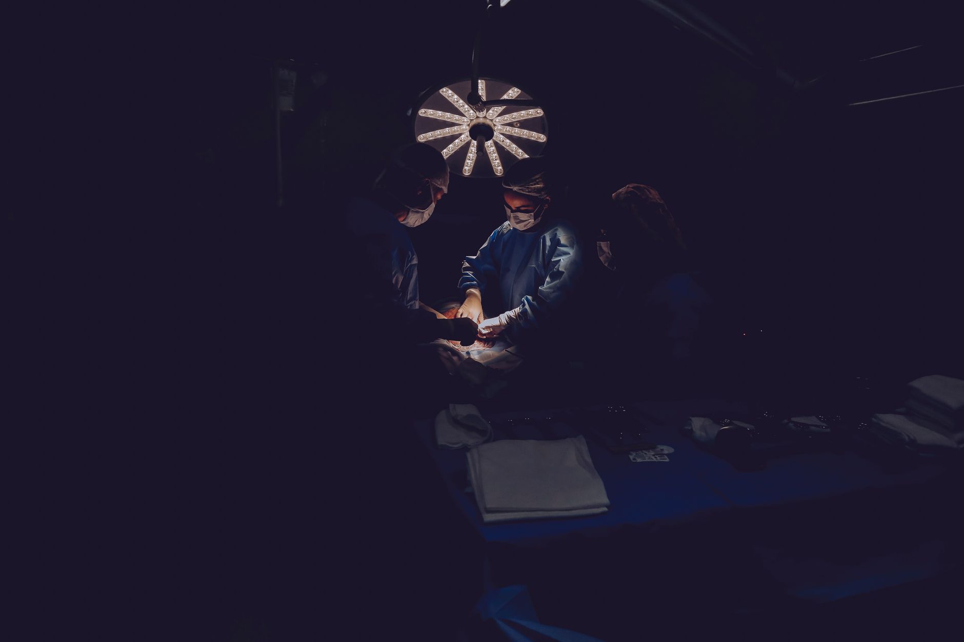 A team of surgeons focuses intently on a procedure in a dimly lit operating room, emphasizing precision and skill.