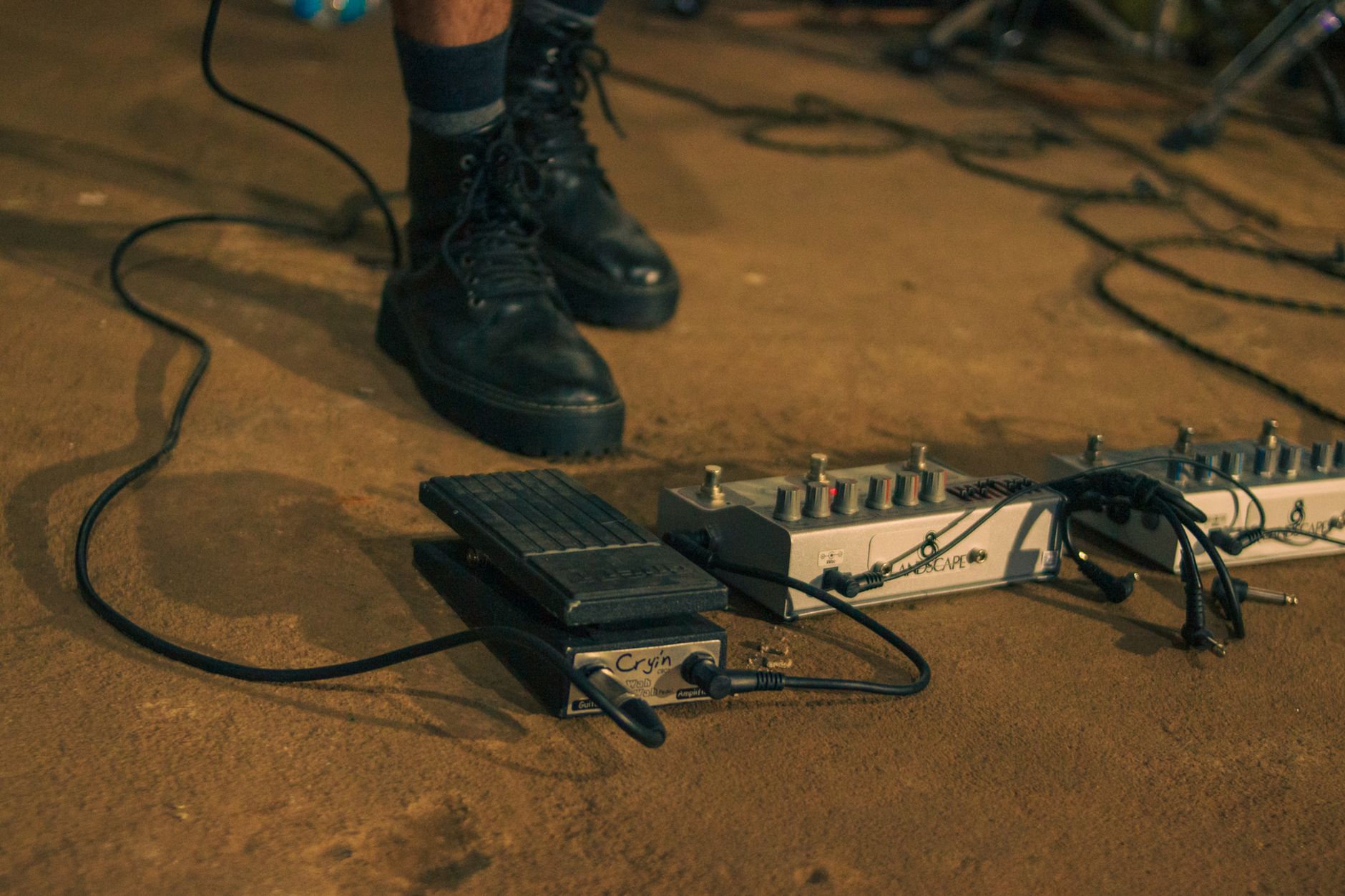 Close-up of a musician's feet on a stage with various guitar effects pedals.
